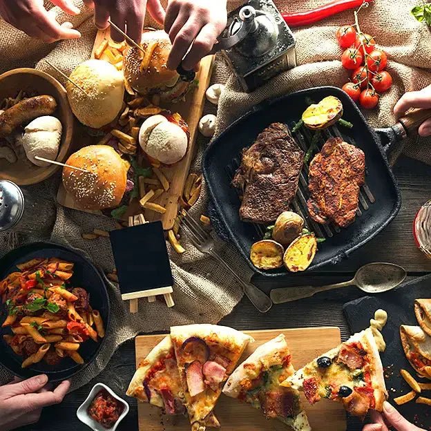Appetizers with various dishes such as burgers, pizza, pasta and cuts of meat, served on the wooden surface and at the table.