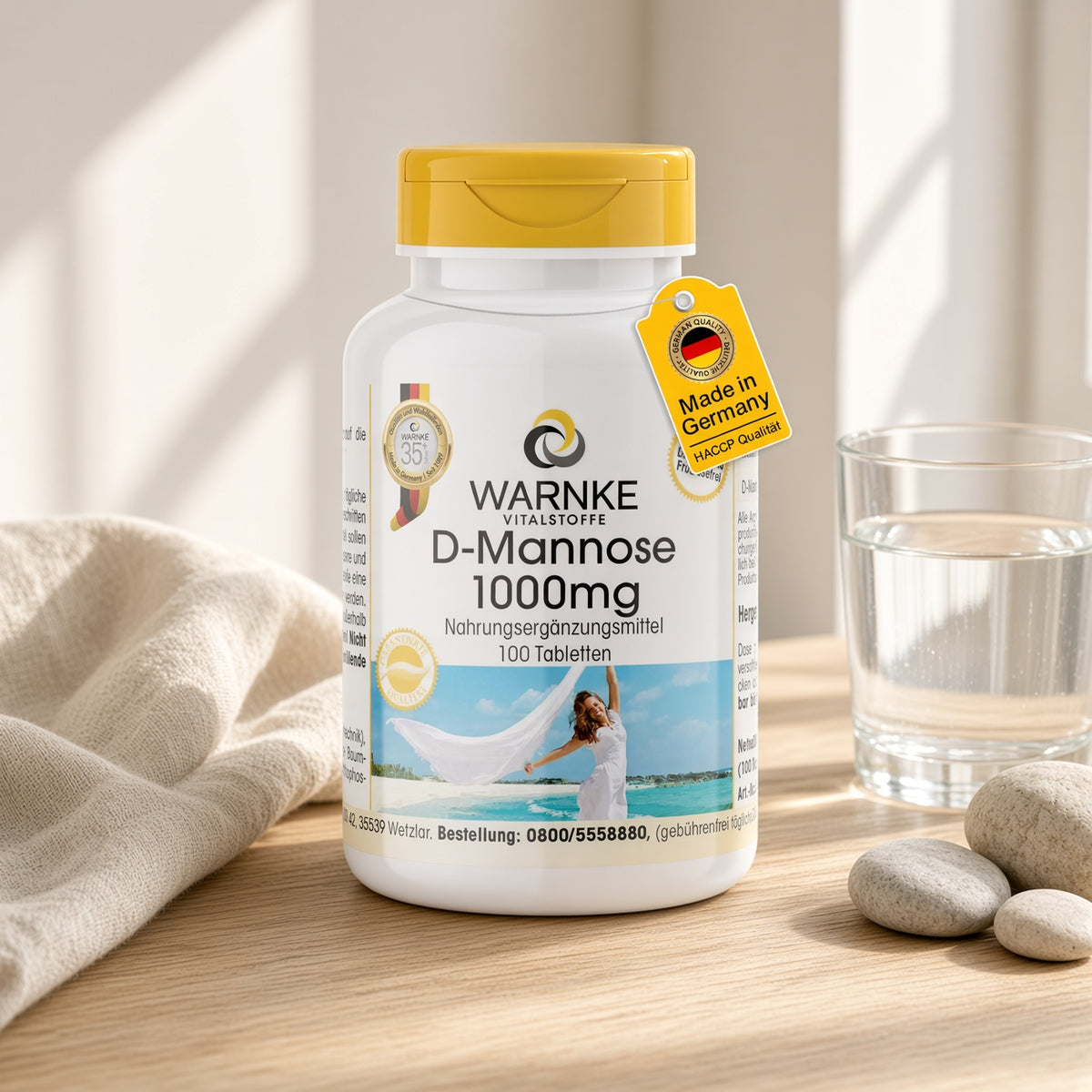 D-Mannose 1000 mg, 100 tabletter i en hvid flaske med gullig låg, placeret på et lyst trægulv ved siden af et glas vand.