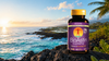 Flacon d'astaxanthine BioAstin Supreme avec étiquette violette, 60 gélules végétaliennes, debout sur des rochers avec fond océan et coucher de soleil.