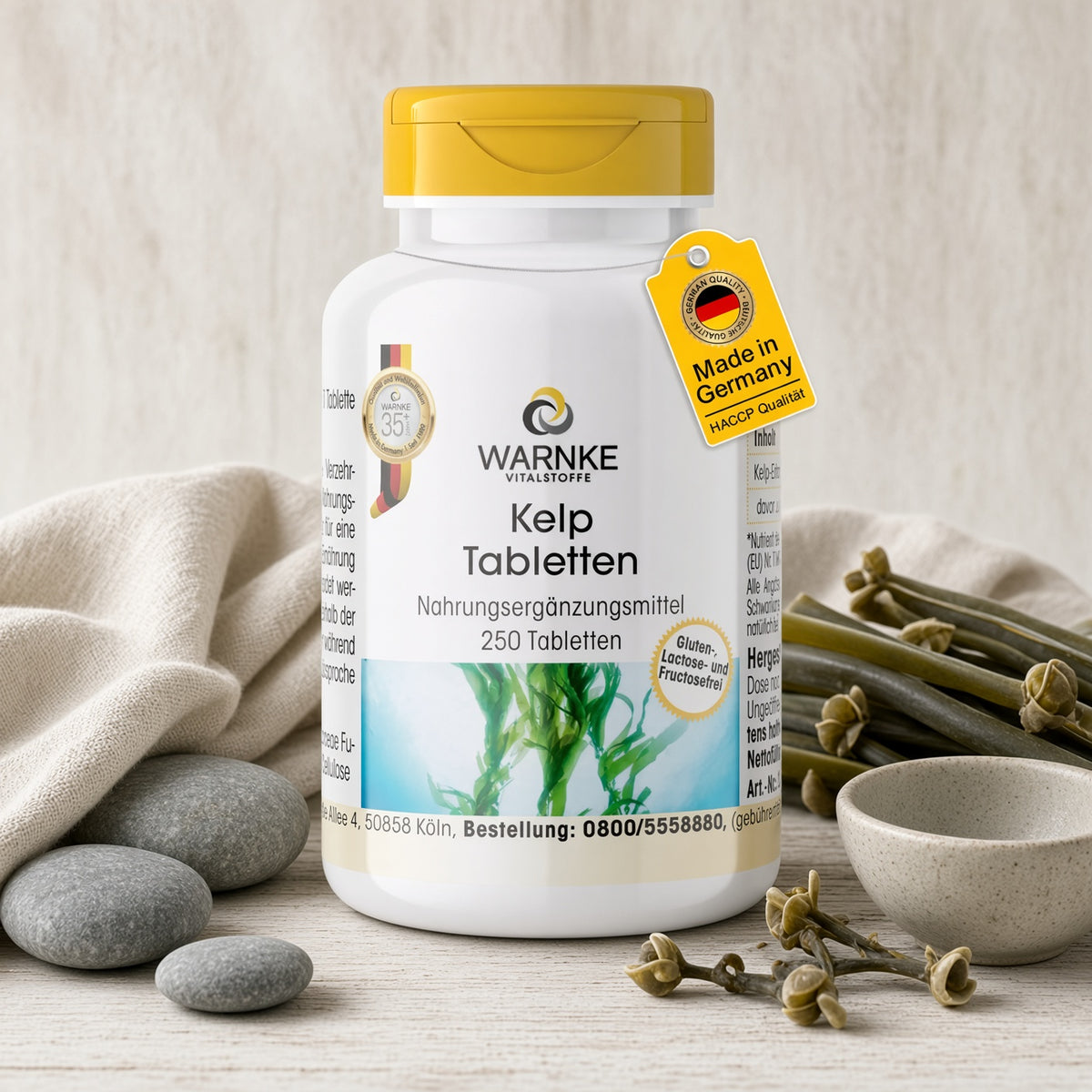 Kelp tabletter i hvid beholder med gult låg, indeholder 250 tabletter. Designet viser tang og sten på et bord.
