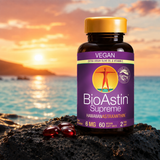 Astaxanthine BioAstin Supreme dans une bouteille en plastique marron avec un bouchon jaune, six gélules rouges sur roche noire, horizon avec coucher de soleil.