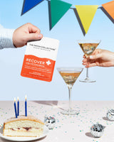 Hand holding a pack of "Recover Patches" in front of a festive background with drinks and cake.
