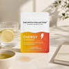 Wellness-plasterpakken "Energy Active Boost" med 15 plastre, i farverig emballage, ved siden af ​​et glas citronvand og en lille skål.