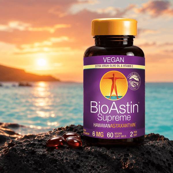 BioAstin Supreme astaxanthin i en brun plastflaska med gult lock, sex röda softgels på svart sten, horisont med solnedgång.