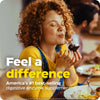 Woman with curly red hair tasting a chocolate dessert, wearing a yellow t-shirt and blue denim pants.