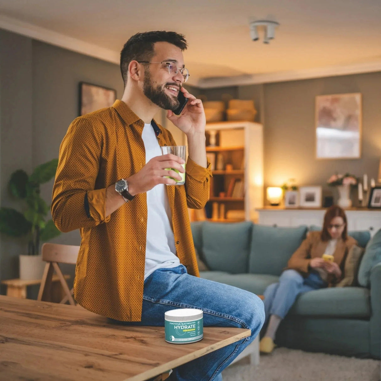 Man with brown shirt holding glass of lime drink in hand, with Go-Keto Hydrate container on table.