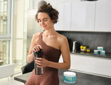 Woman in brown workout clothes mixes Go-Keto electrolyte powder in a shaker on the kitchen counter.