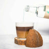 Clear glass cup of coffee, into which Go-Keto MCT oil is poured from a transparent bottle, next to a coconut.
